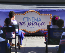 Crianças sentadas com o banner do projeto Cinema na Praça logo a frente