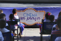 Crianças sentadas com o banner do projeto Cinema na Praça logo a frente