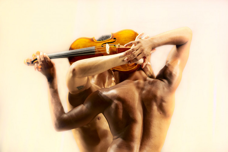 Dois homens com torços nus se abraçam segurando um violino