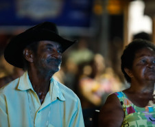 Um homem de chapéu preto e camisa clara assistindo o cinema junto de uma mulher de vestido colorido