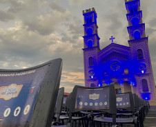 Cadeiras do projeto Cinema na Praça com uma igreja iluminada de azul ao fundo