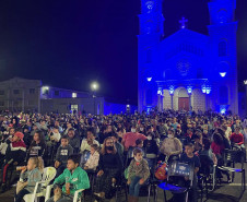 Pessoas assistindo cinema em uma praça com uma igreja ao fundo