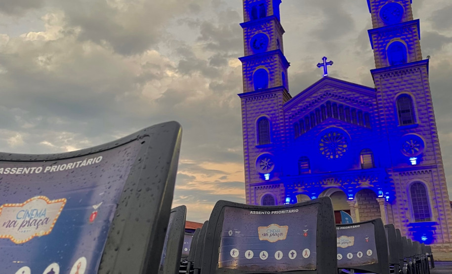 Cadeiras do projeto Cinema na Praça com uma igreja iluminada de azul ao fundo