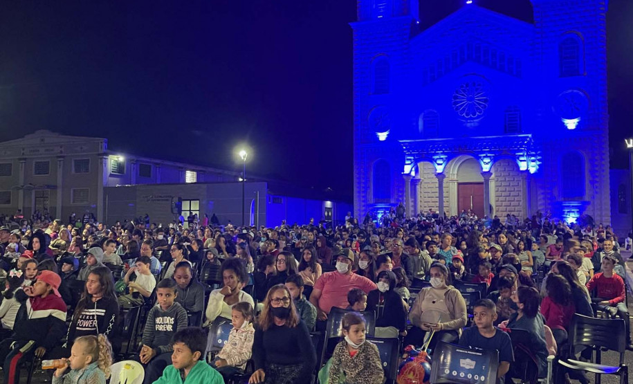 Pessoas assistindo cinema em uma praça com uma igreja ao fundo